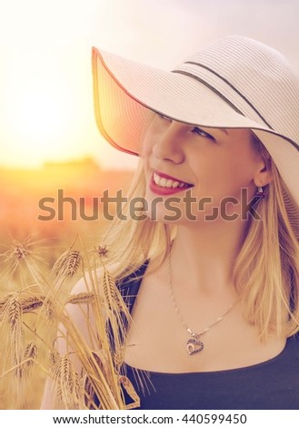 Beautiful young woman posing in the field with sunset in background. Filter used on photo
