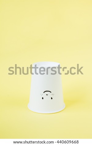 Drawing cute face on white paper coffee cup  on yellow background. Side light.
