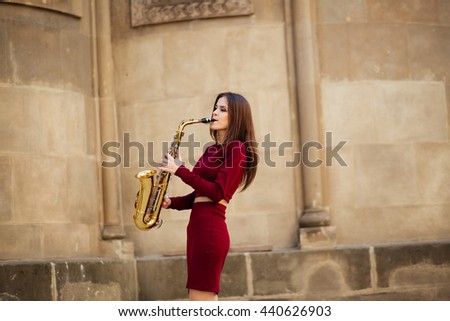 portrait of a beautiful young girl walking on the street with a saxophone