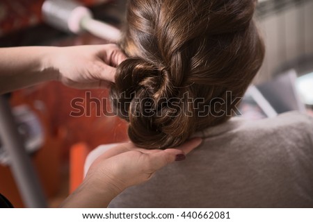 Closeup picture of beautiful lady sitting in chair and looking at mirror while hairdresser making braid in hairdressing saloon.