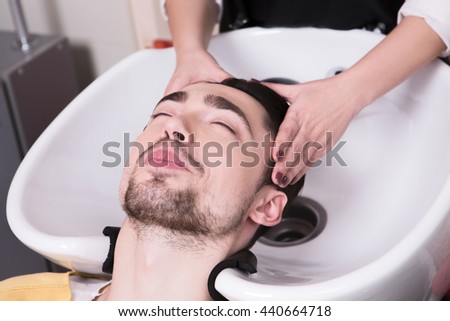 Close up picture of young man lying with his eyes closed in beauty saloon while having his hair washed in hairdressing saloon.