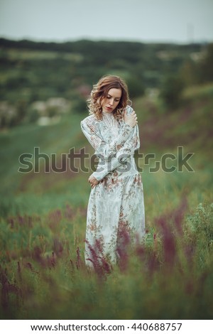 Young girl in vintage dress walking through sage flower field. 