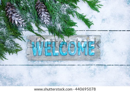 Winter welcome sign with tree branch and pine cones border on teal blue snowy wooden background