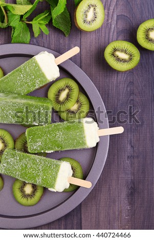 Homemade kiwi popsicles on a plate with mint and kiwi slices on a dark wooden table. Top view with copyspace