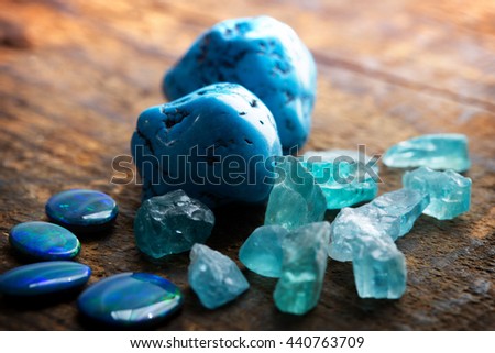 Treasure hunting. Mining for gems. Blue gems on rustic wooden table. Blue Turquoise, blue opals and apatite stones on a wooden table. Focus on large turquoise stone. Shallow depth of field.