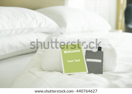 Welcome card placed inside a hotel room bed with White towel and card room door.