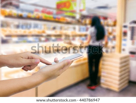 Girl use mobile phone, blur image of inside bread shop as background.