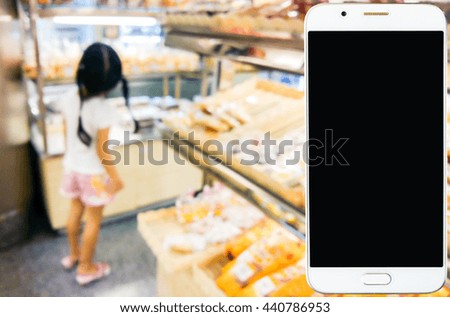 Girl use mobile phone, blur image of inside bread shop as background.