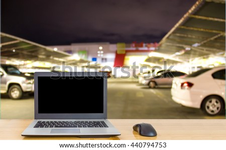 Computer on the table, blur image of parking lot as background.