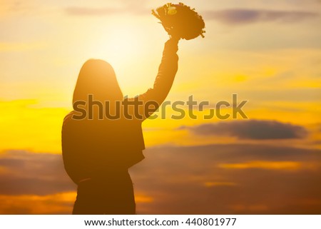 Silhouette of happy young woman hold bouquet of flower over beautiful twilight sunset.