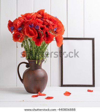Red poppies bouquet in clay jug with motivational frame  for your text or picture on background of white wooden planks in scandinavian style