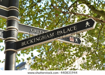 London Buckingham Palace direction signpost near Hyde Park Corner with green tree branches in the background.
Direction signpost to British Queen London residence The Buckingham Palace.
