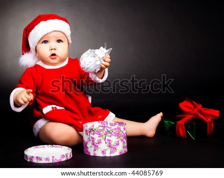 studio portrait of a happy baby dressed as Santa with presents
