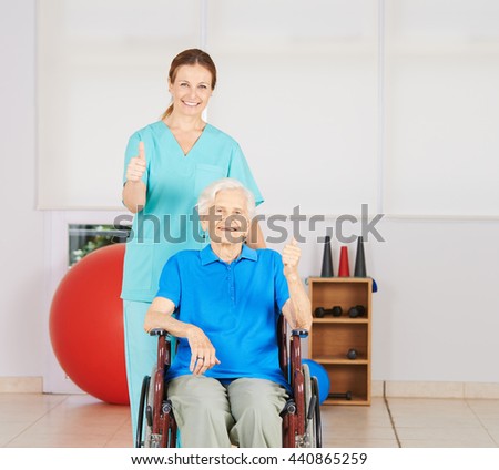 Happy old woman in wheelchair holding her thumbs up with geriatric nurse