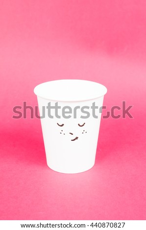 Drawing cute face on white paper coffee cup on red  background. Side light.