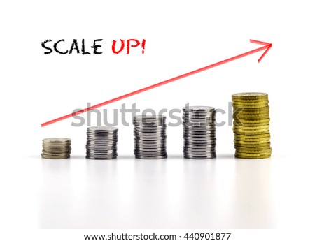 Conceptual image. Stacks of coins against white background with red arrow and SCALE UP words.