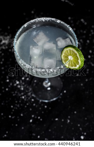 Classic mexican margarita cocktail on black background. Margarita glass full of ice, salt and lime on side. Black background with whites sea salt spots.