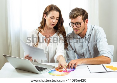 Male and female collegues discussing colour samples at desk in creative office