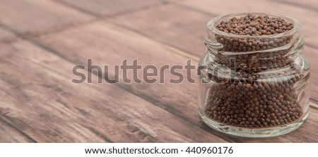 Brown Indian mustard seed in mason jar over wooden background