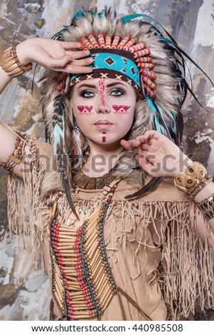 Expressive young girl with a pattern on the face and feathers and Roach looks directly into ethnic national style North American Indian background hairstyle and makeup close-up portrait