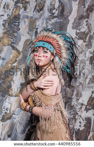 Expressive young girl with a pattern on the face and feathers and Roach looks directly into ethnic national style North American Indian background hairstyle and makeup