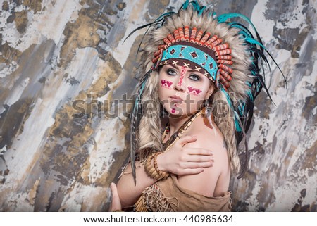 Expressive young girl with a pattern on the face and feathers and Roach looks directly into ethnic national style North American Indian background hairstyle and makeup close-up portrait