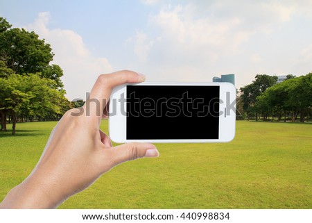 Hand holding smart phone on City park under blue sky with building background