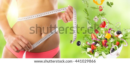 Slim girl measuring her waist with salad in motion.