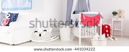 Panoramic picture of a white modern nursery with blue and red accessories