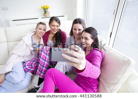 Four woman are sat at home in their pajamas talking a selfie. They are drinking champagne and smiling.