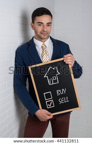 Man in a suit with a black board in his hands on a white background. Drawn the house and motivational text.