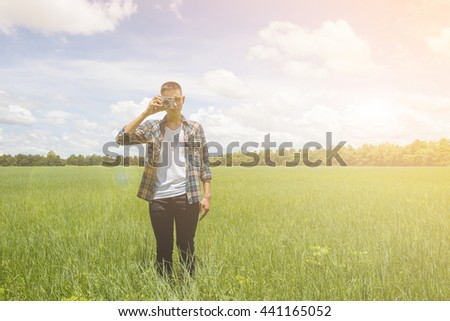 Young man with camera at meadow against sky.Man standing on green grass background