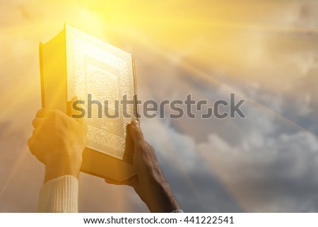 Man's hands holds Koran - holy book of muslims, on blue sky with clouds. With instagram style filter Royalty-Free Stock Photo #441222541