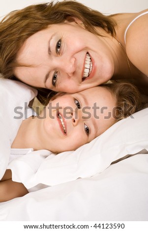 Big smiles in the morning - closeup of woman and little girl grinning, laying in the bed