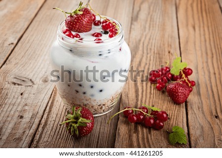 Yogurt dessert with muesli and fresh red currant and strawberry on wooden table