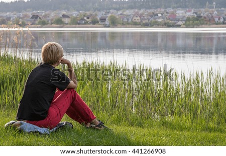 A middle-aged woman sitting on the grass by the lake.