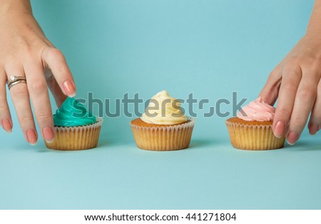Closeup photo of female hands choosing between three colorful cupcakes over blue background