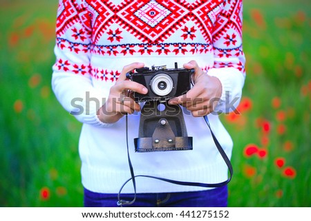 Retro photo camera in hands of women at green background, national pattern svitshot, pullover 