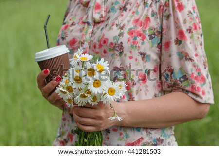 Hand holding paper cup of coffee on natural summer grass background