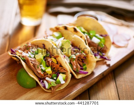three  pork carnitas street tacos in yellow corn tortilla with avocado, onion, cilantro and cabbage