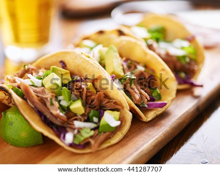 three  pork carnitas street tacos in yellow corn tortilla with avocado, onion, cilantro and cabbage Royalty-Free Stock Photo #441287707