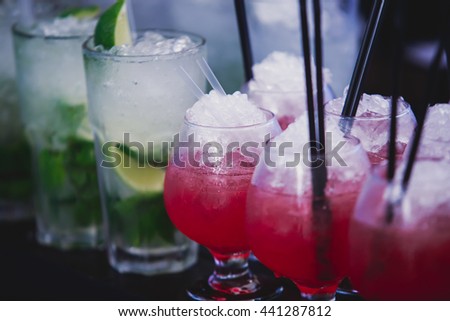 Beautiful row line of different colored alcohol cocktails with mint on a party, martini, vodka,and others on decorated catering bouquet table on open air beach event