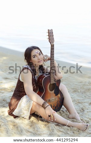 a girl in style of bokho plays on a guitar  musician music street on a beach clothes style accessories makiyazh mekhendi picture by a henna hippie summer beach sand bangle of necklace