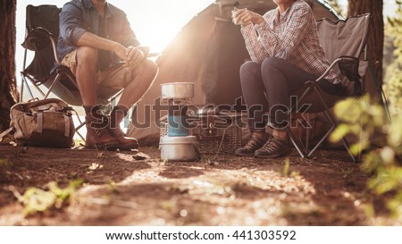 Cropped image of man and woman sitting in chairs outside the tent. Couple camping in forest. Royalty-Free Stock Photo #441303592