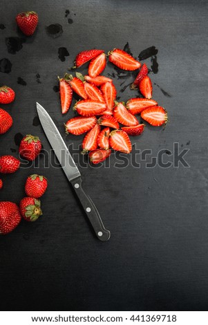 whole and sliced strawberries and knife on black background with copyspace