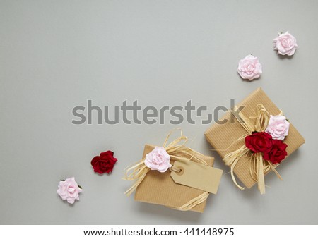 Presents wrapped in brown parcel paper with raffia bows, a blank gift label and pink and red roses on a grey background forming a page border