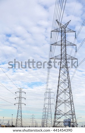 high voltage tower and electricity pylon silhouette against blue sky and clouds in background