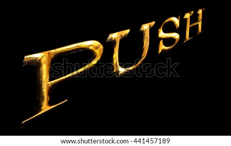Wooden letters in gold on black background spelling PUSH