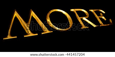 Wooden letters in gold on black background spelling MORE