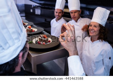 Head chef showing ok hand sign after inspecting dessert plates in restaurant